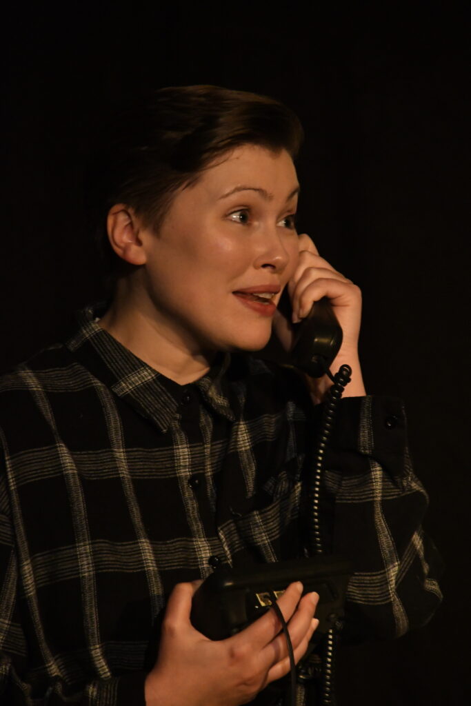 A photo of a person on stage holding the handset of an old style phone